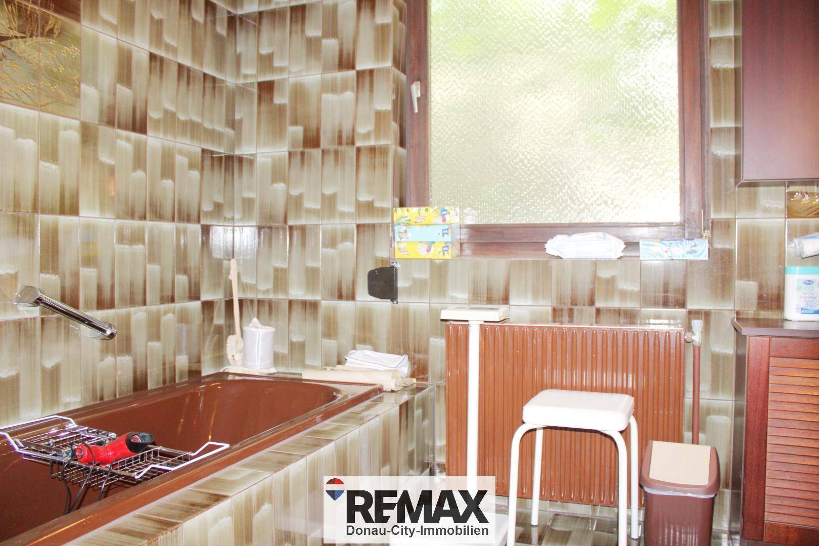 Badezimmer im 80er-Jahre-Stil mit braunen Fliesen, Badewanne und Fenster.