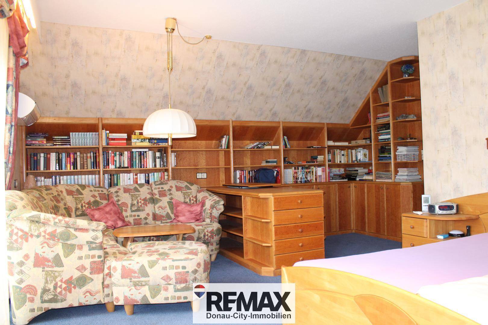 Geräumiges Schlafzimmer im Dachgeschoss mit Teppichboden, Bücherregalen und einem Schreibtisch.