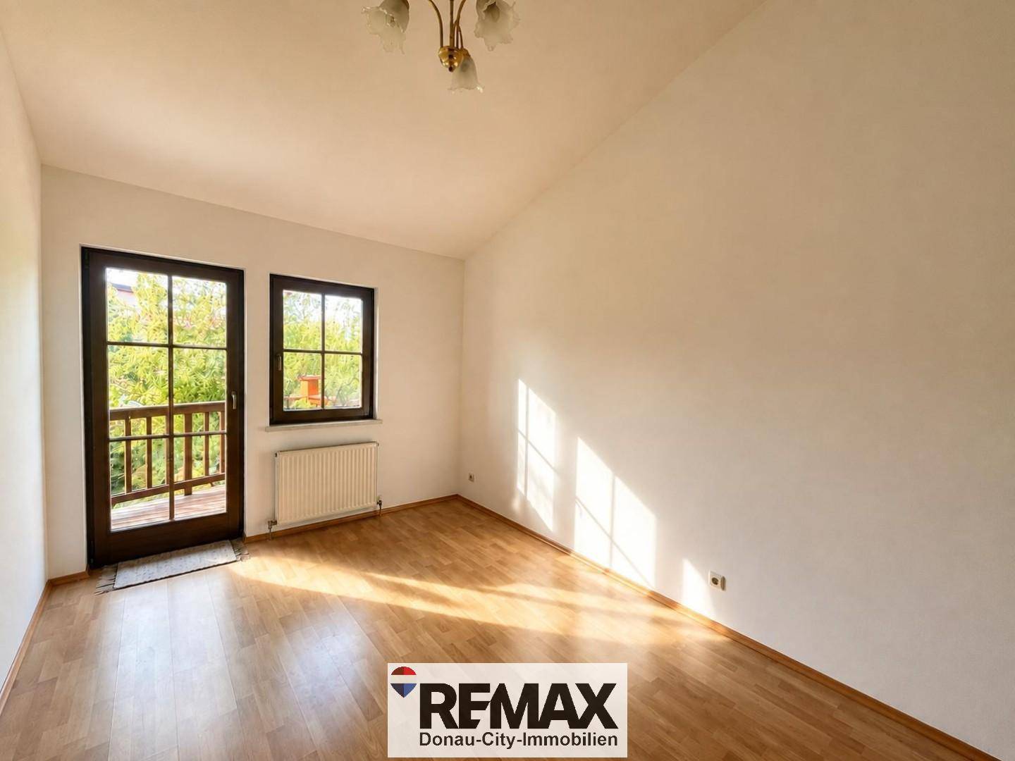 Helles Zimmer mit Holzboden und Zugang zu einem kleinen Balkon, ideal als Schlaf- oder Gästezimmer.