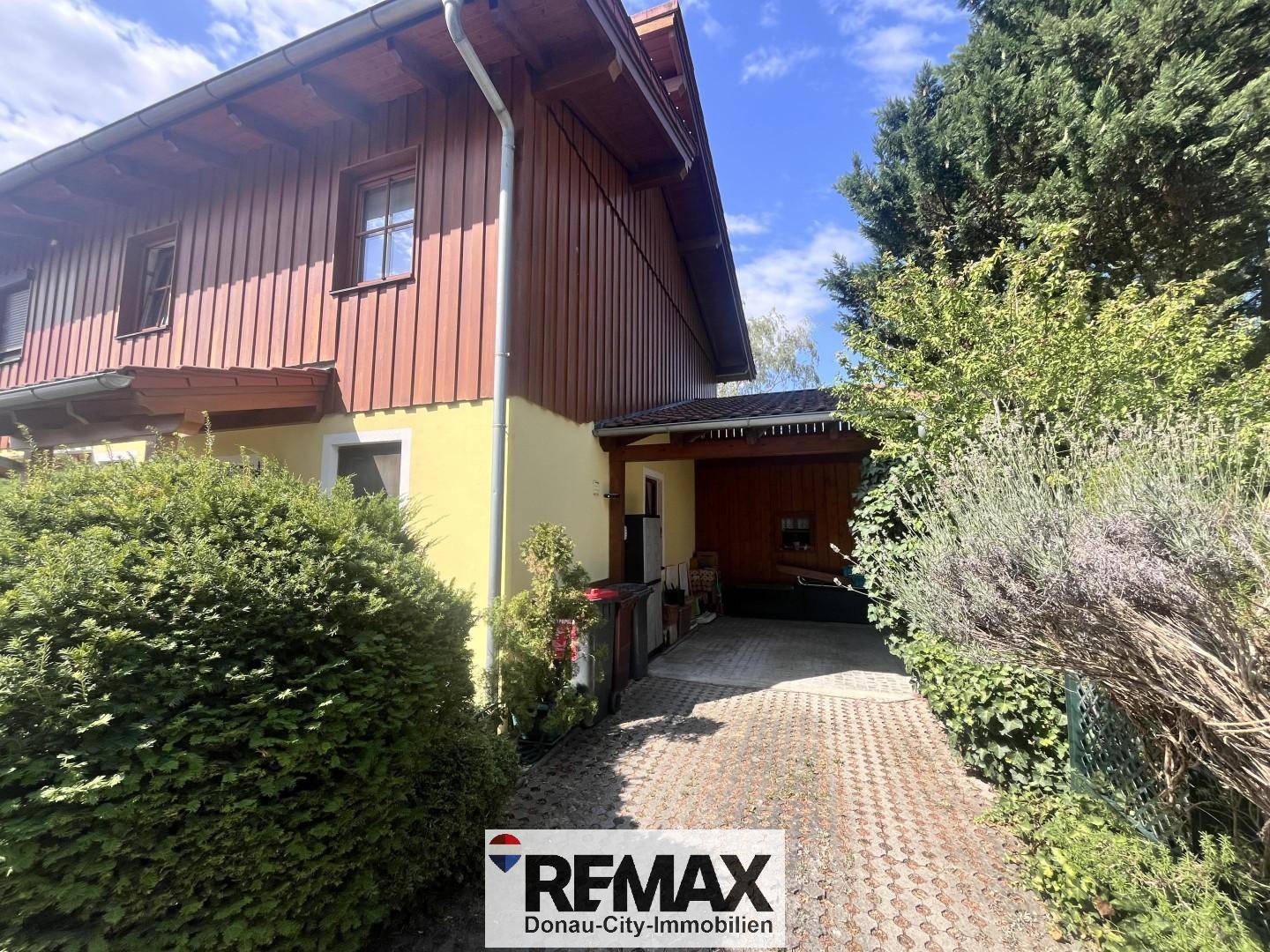 Außenansicht eines gepflegten Hauses mit Holzfassade, gepflasterter Einfahrt und Carport.