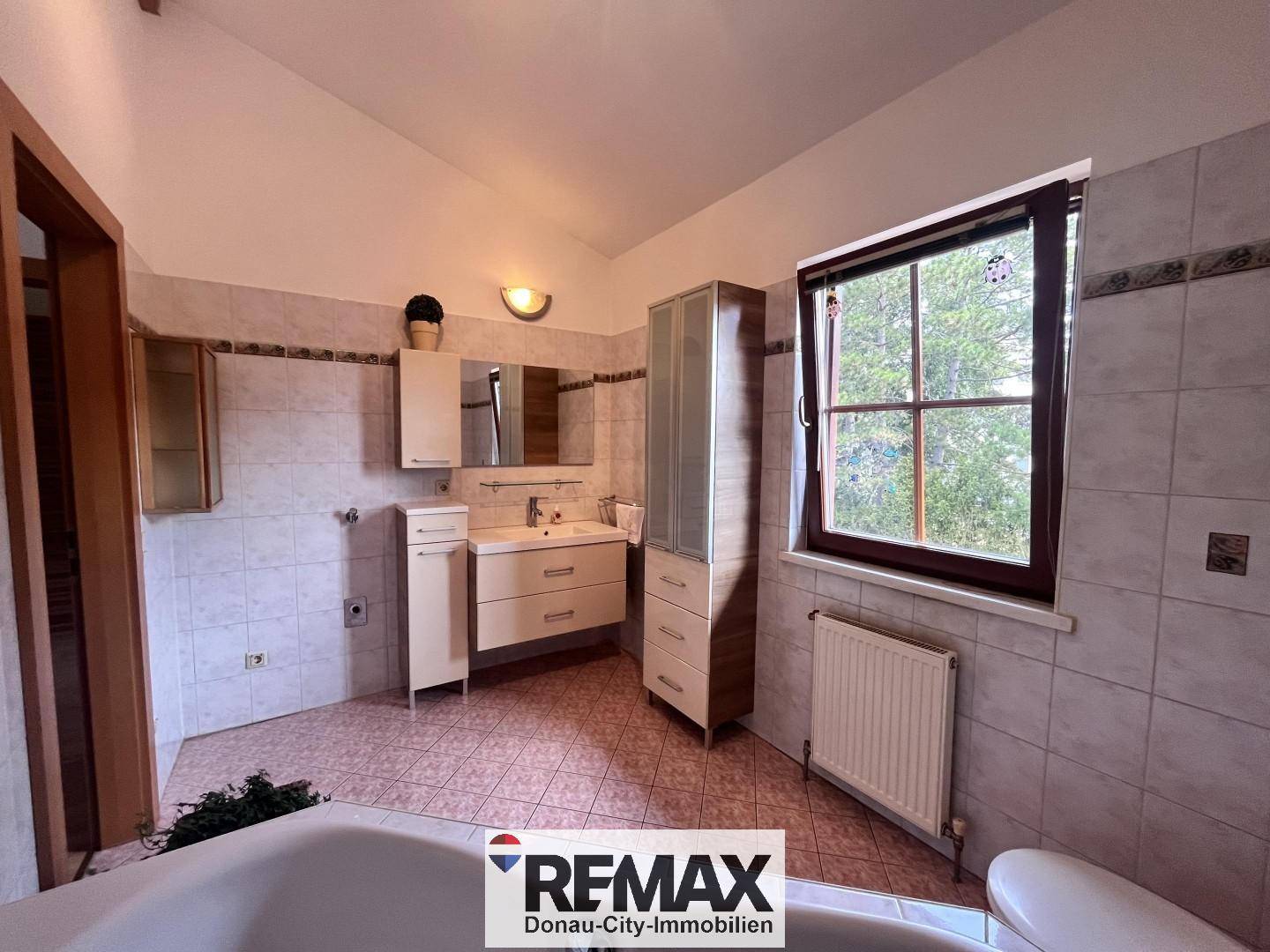 Badezimmer mit Badewanne, Waschtisch und hellen Fliesen, gut beleuchtet.