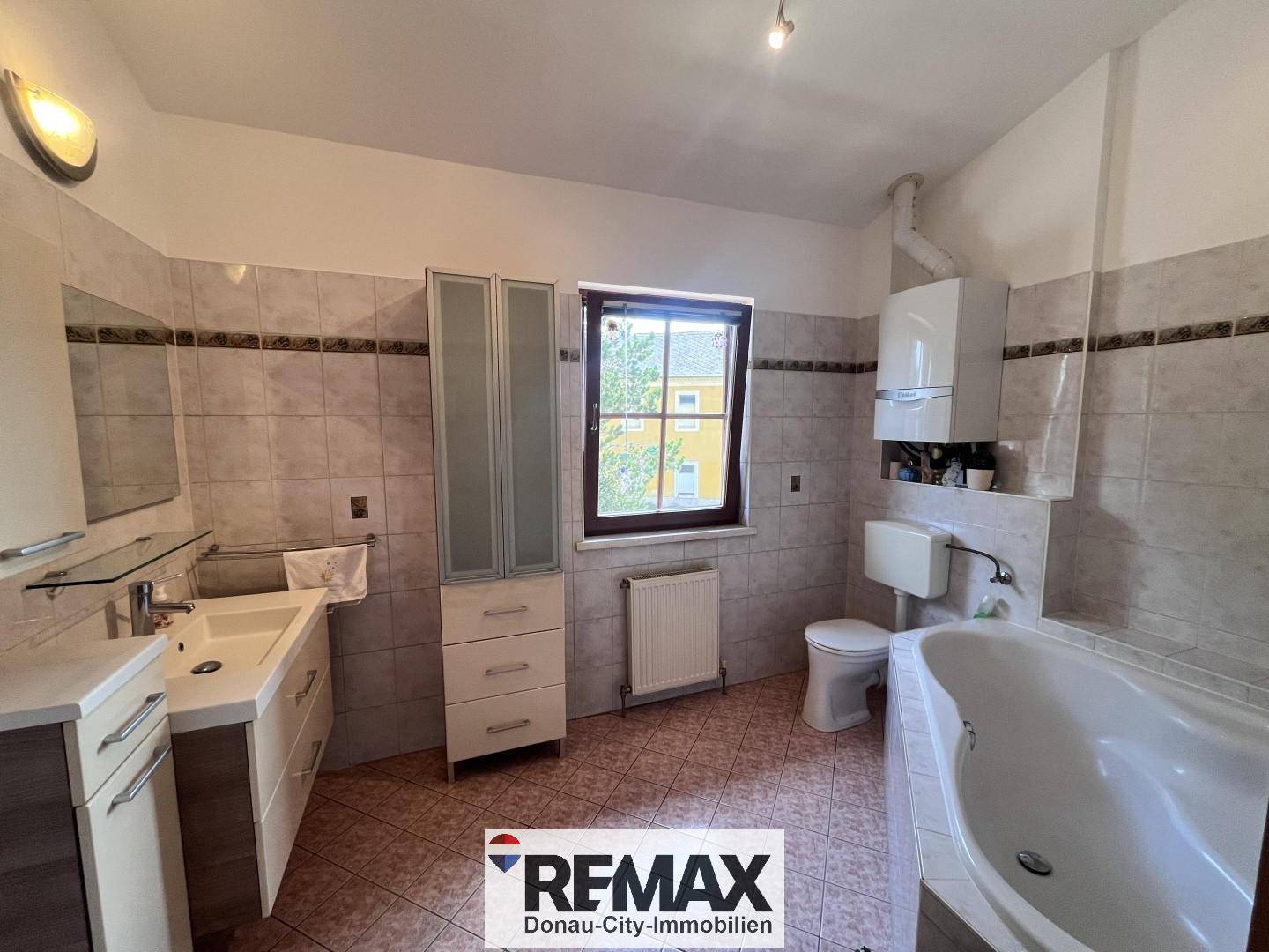 Geräumiges Badezimmer mit Badewanne, Waschtisch und Fenster.