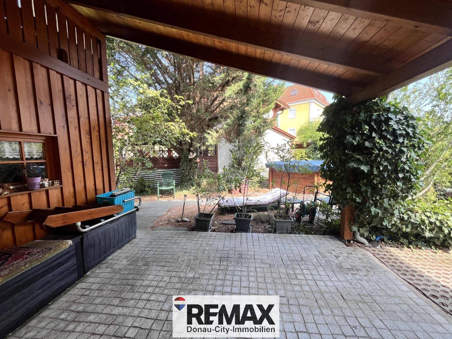Überdachte Terrasse mit gepflastertem Boden und Blick in den grünen Garten.