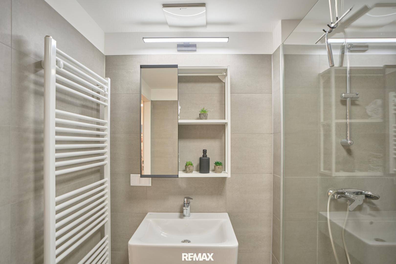 Elegantes Badezimmer mit grauen Fliesen, Handtuchwärmer und moderner Duschkabine mit Glasabtrennung.