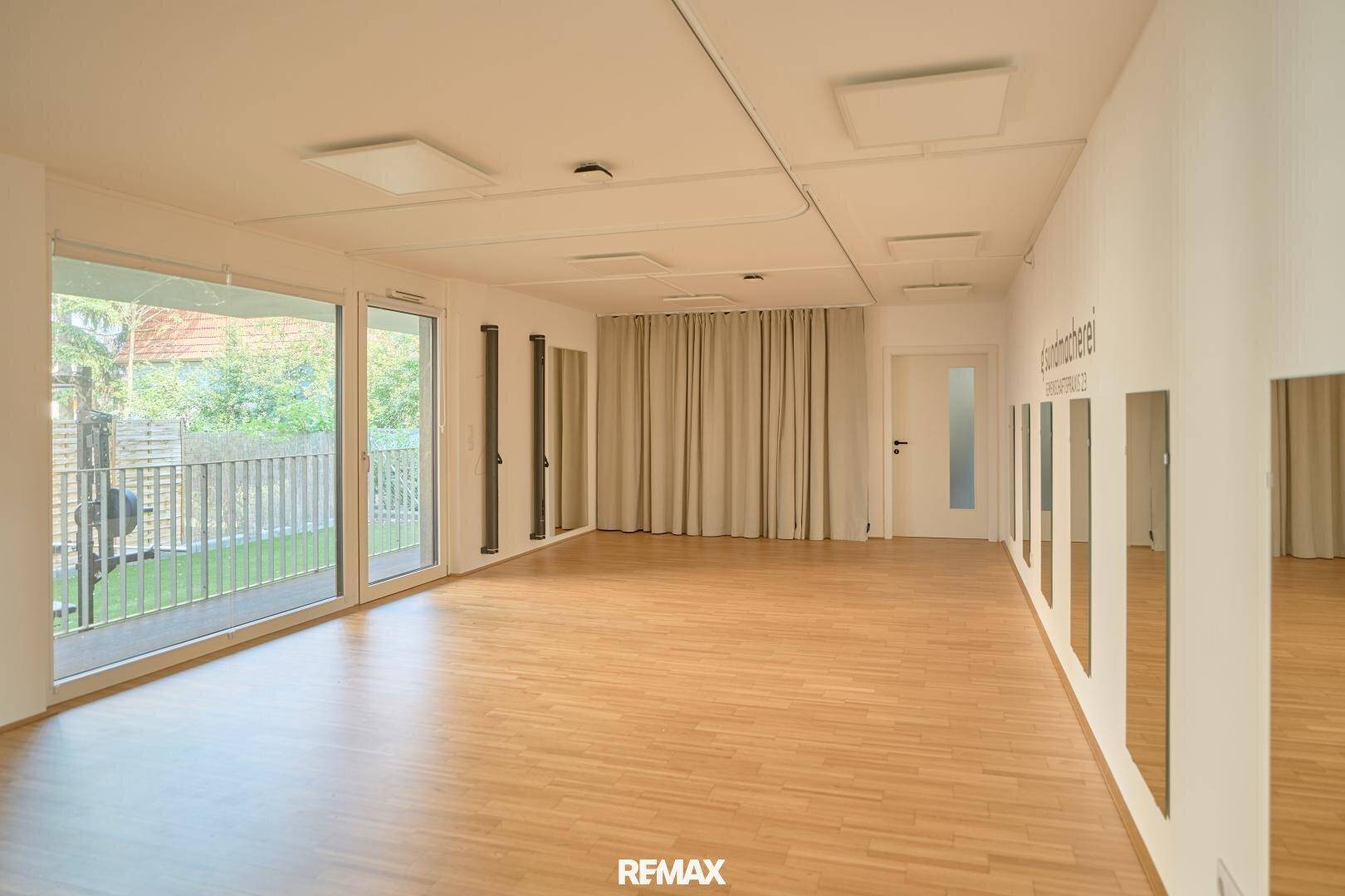 Geräumiger Studiobereich mit hellem Holzfußboden, großen Glasfronten und Blick auf den Außenbereich.
