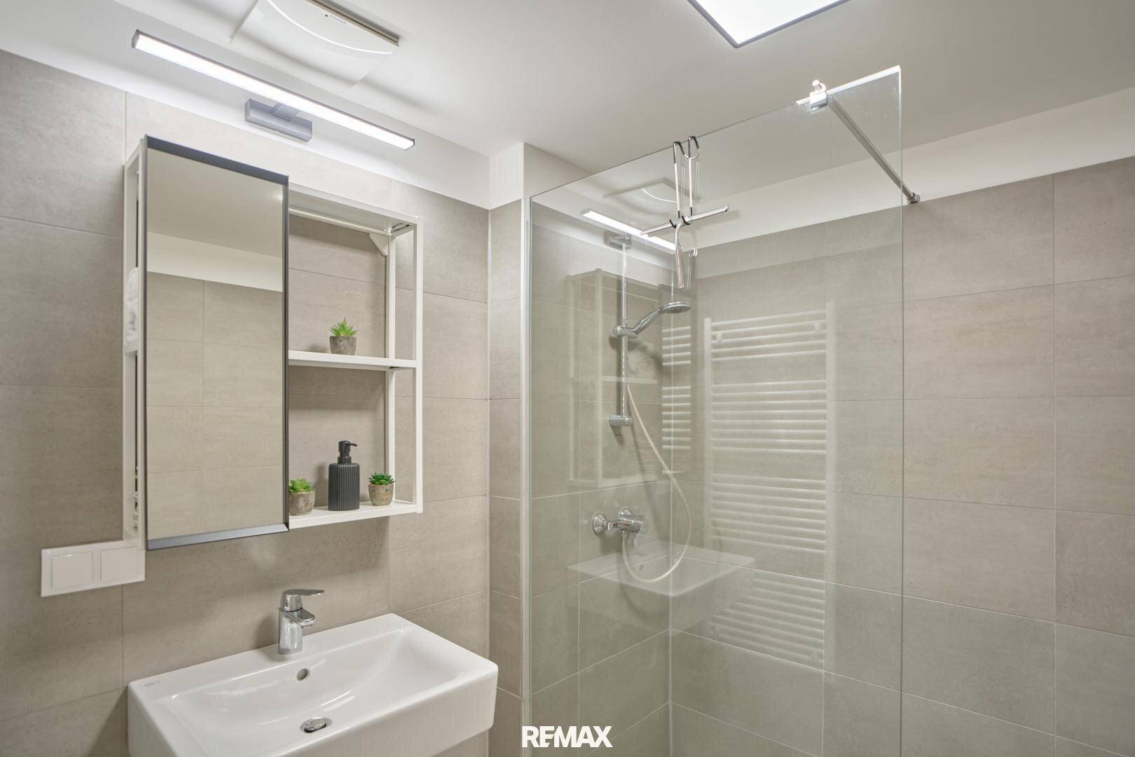 Modernes Badezimmer mit grauen Fliesen, begehbarer Dusche und stilvollem Waschtisch mit Spiegelschrank.