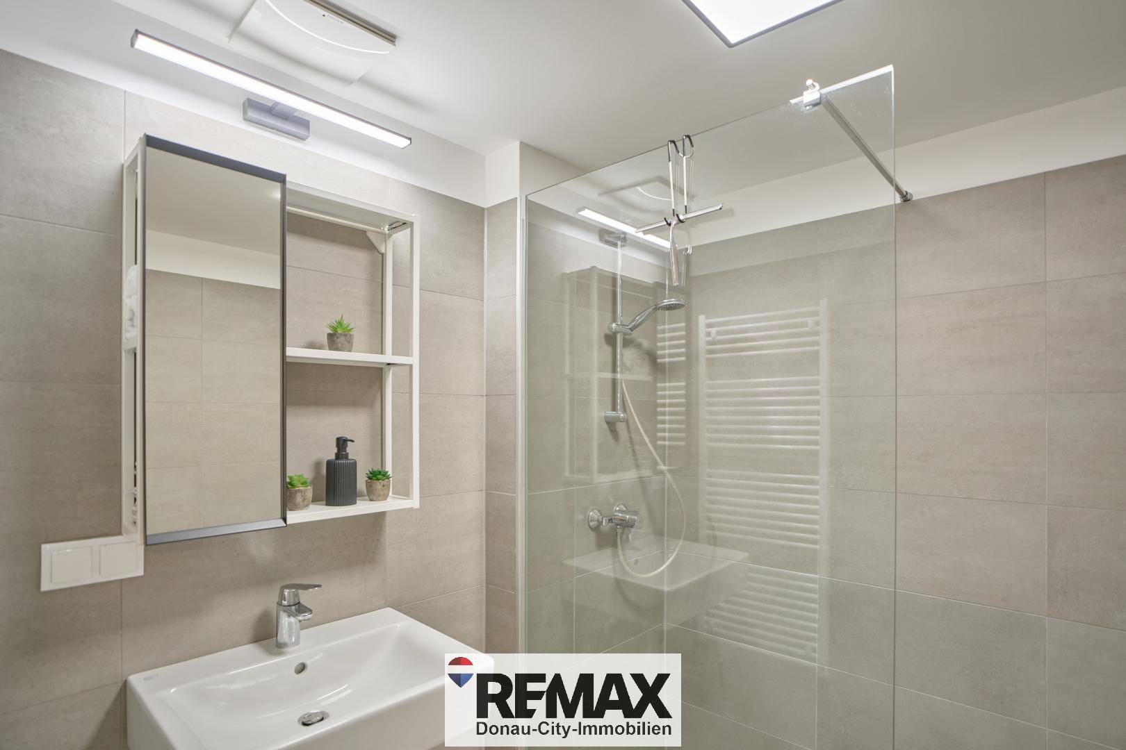 Modernes Badezimmer mit grauen Fliesen, Waschtisch, Spiegelschrank und einer begehbaren Dusche.