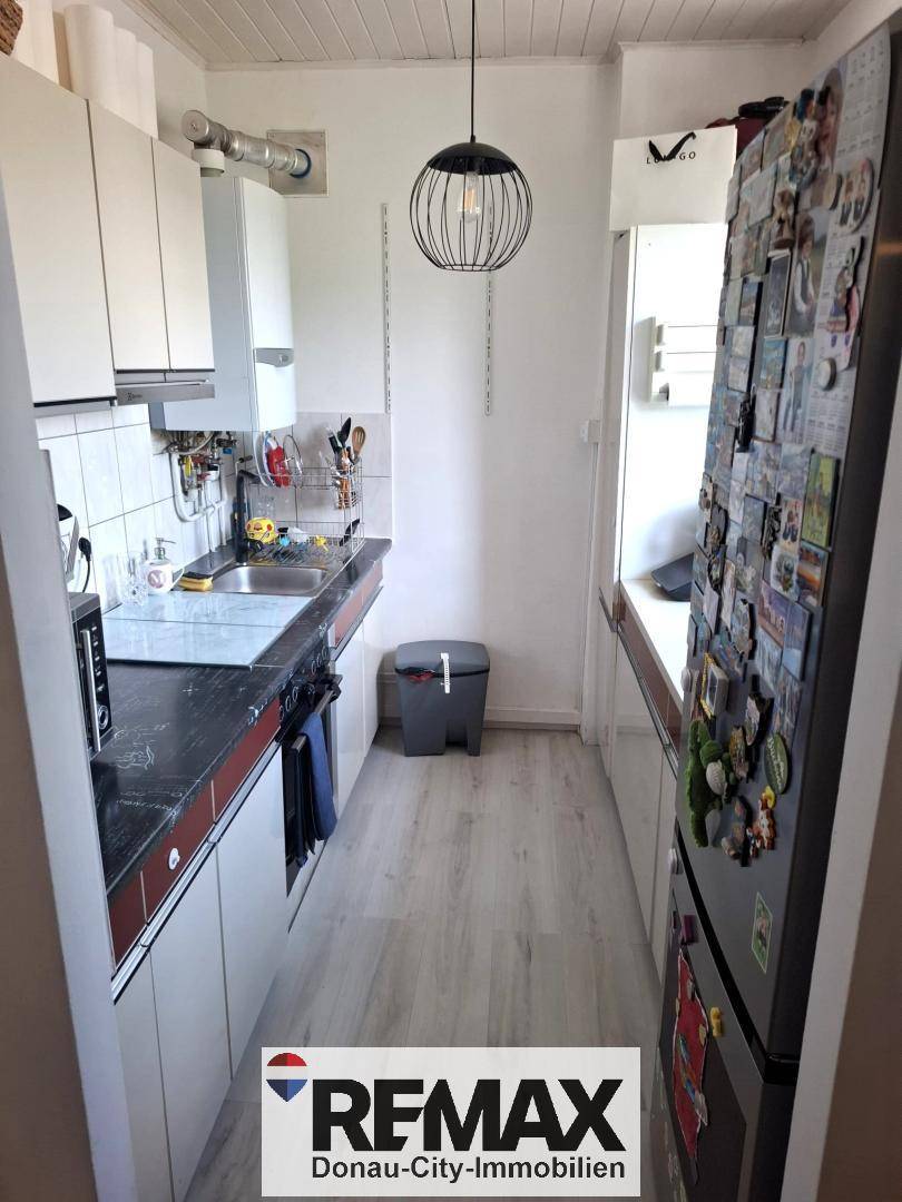 Schmale Küche mit weißen Schränken, dunkler Arbeitsplatte und Kühlschrank.