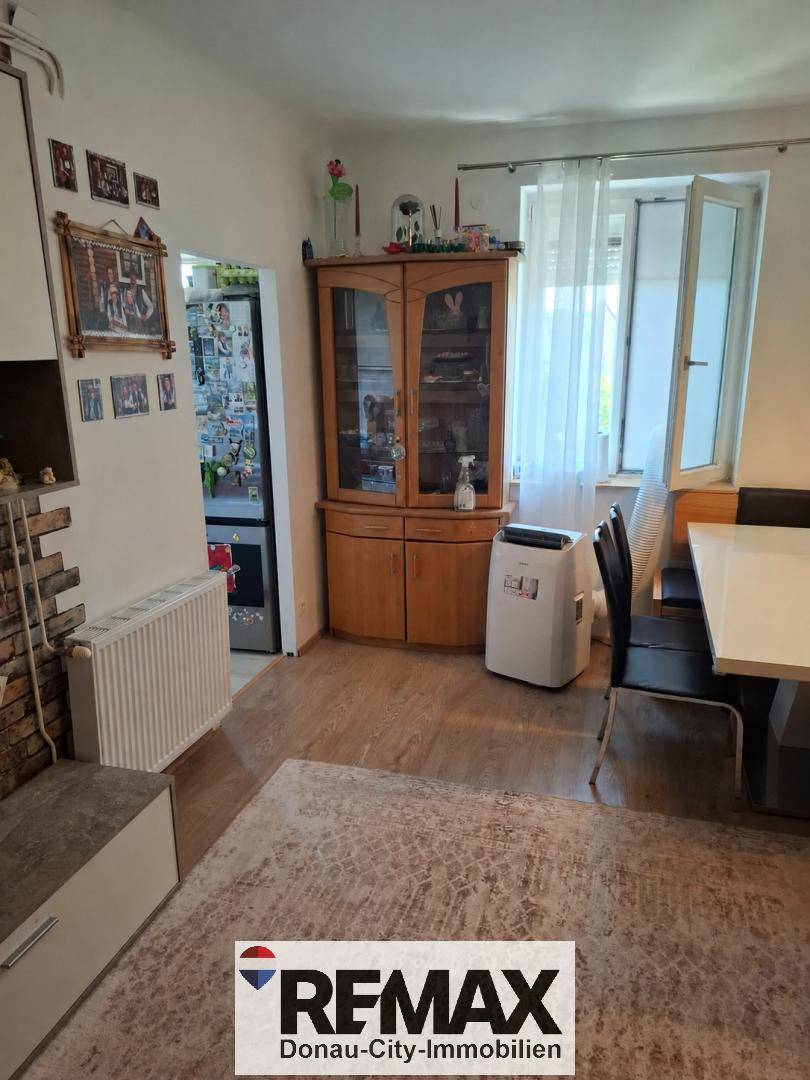 Wohn-Essbereich mit Esstisch, Holzschrank und Fenster mit Vorhängen.
