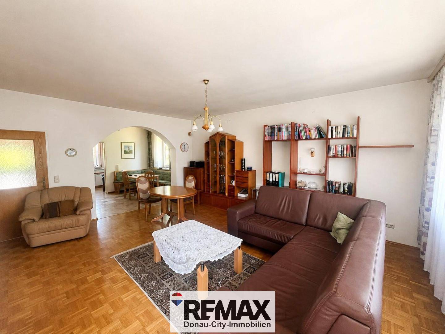 Geräumiges Wohnzimmer mit Parkettboden, Ledersofa und Blick in den angrenzenden Essbereich.