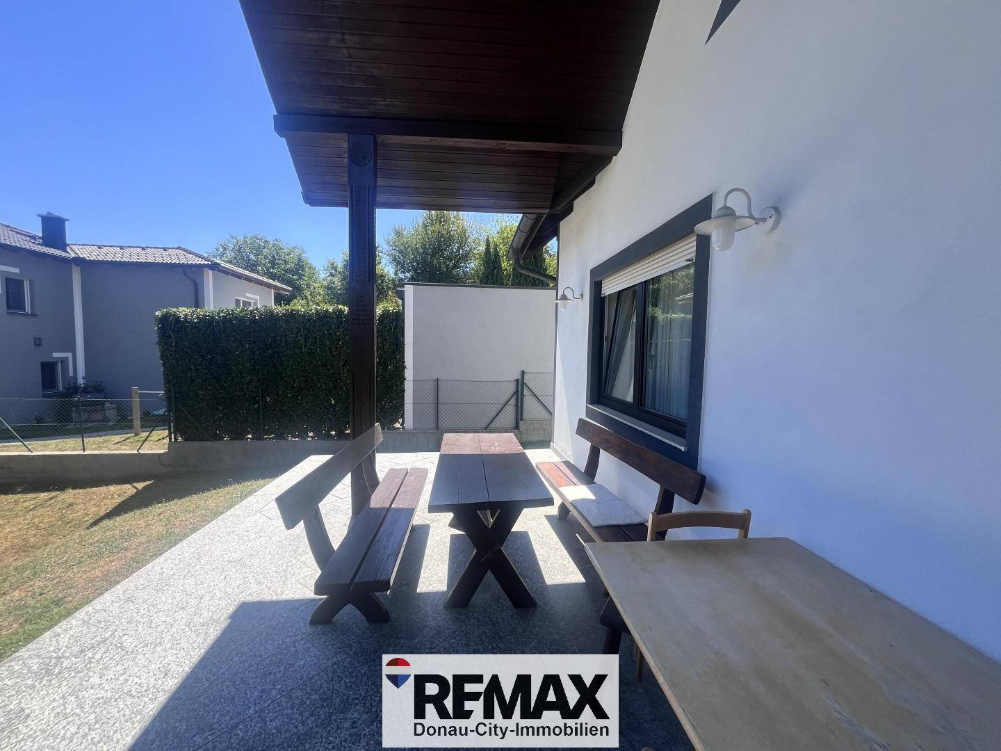 Gemütliche Terrasse mit Holztisch und Bänken, umgeben von Grünflächen.