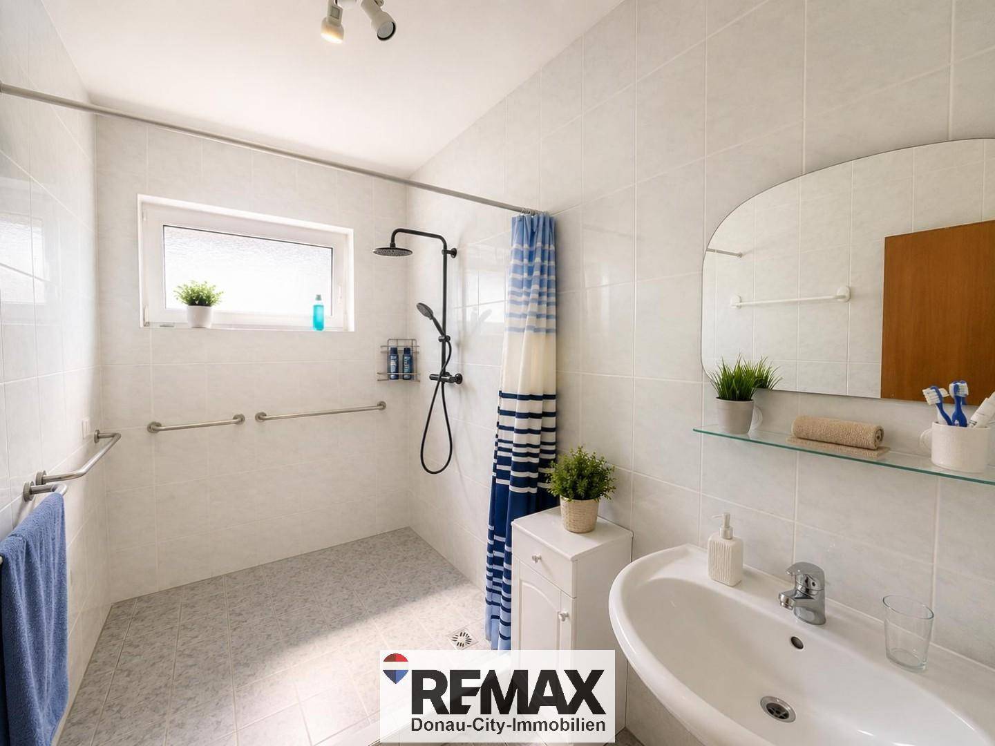 Modernes Badezimmer mit ebenerdiger Dusche, weißen Fliesen und Haltegriffen für Barrierefreiheit.
