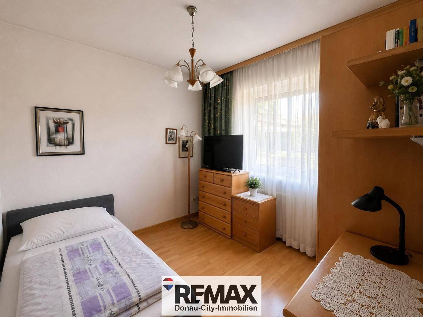 Kinder- oder Gästezimmer mit Einzelbett, Holzmöbeln und Fenster mit Blick ins Grüne.