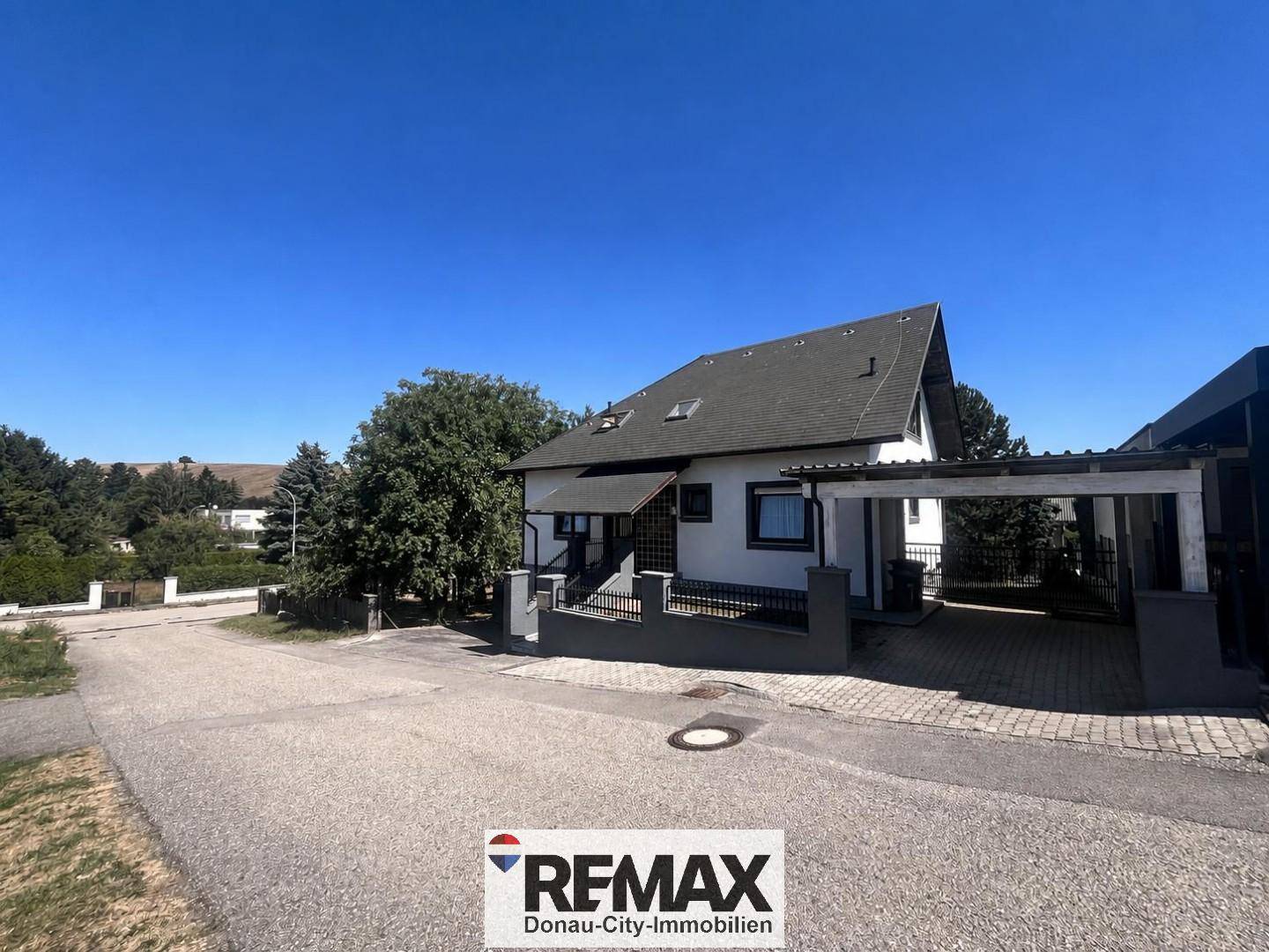 Ansicht des Hauses von der Straße mit Carport und umgebender Landschaft.