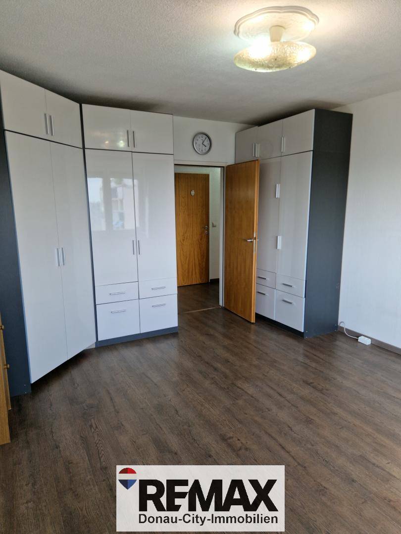 Schlafzimmer mit glänzenden weißen Einbauschränken und dunklem Laminatboden, gut beleuchtet.