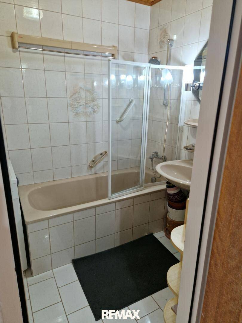Badezimmer mit Badewanne, Duschabtrennung, Waschbecken und hellen Fliesen an Wänden und Boden.