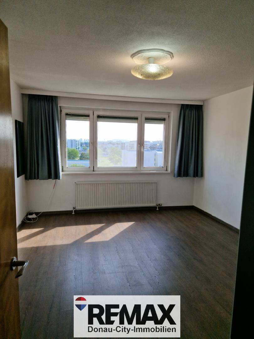 Heller Raum mit dunklem Laminatboden, großem Fenster und Heizkörper, vielseitig nutzbar.