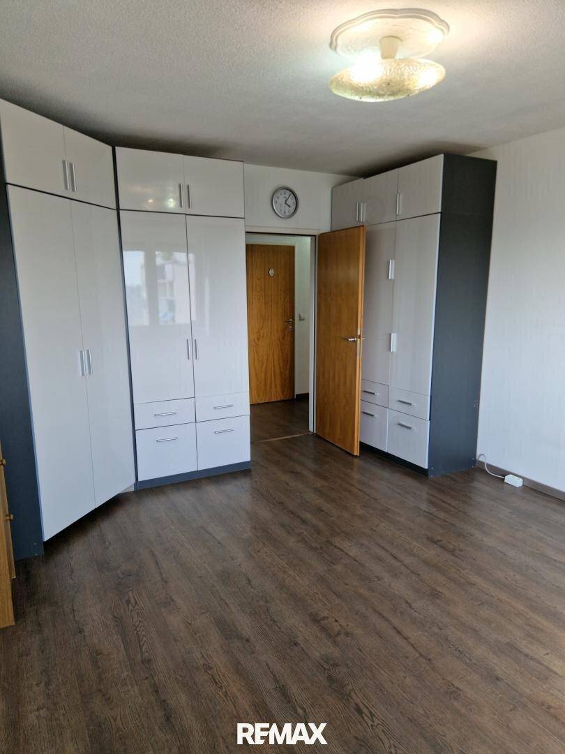Schlafzimmer mit geräumigen weißen Einbauschränken und dunklem Laminatboden, bietet viel Stauraum.