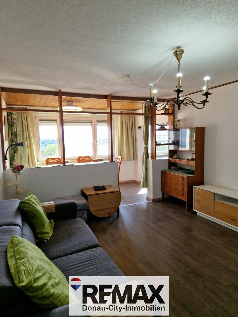 Gemütliches Wohnzimmer mit dunklem Laminatboden, Holzdecke und Blick in einen angrenzenden Bereich.