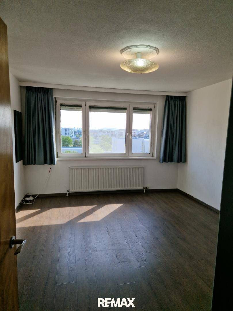Helles Schlafzimmer mit Laminatboden und großem Fenster, das viel Tageslicht hereinlässt.