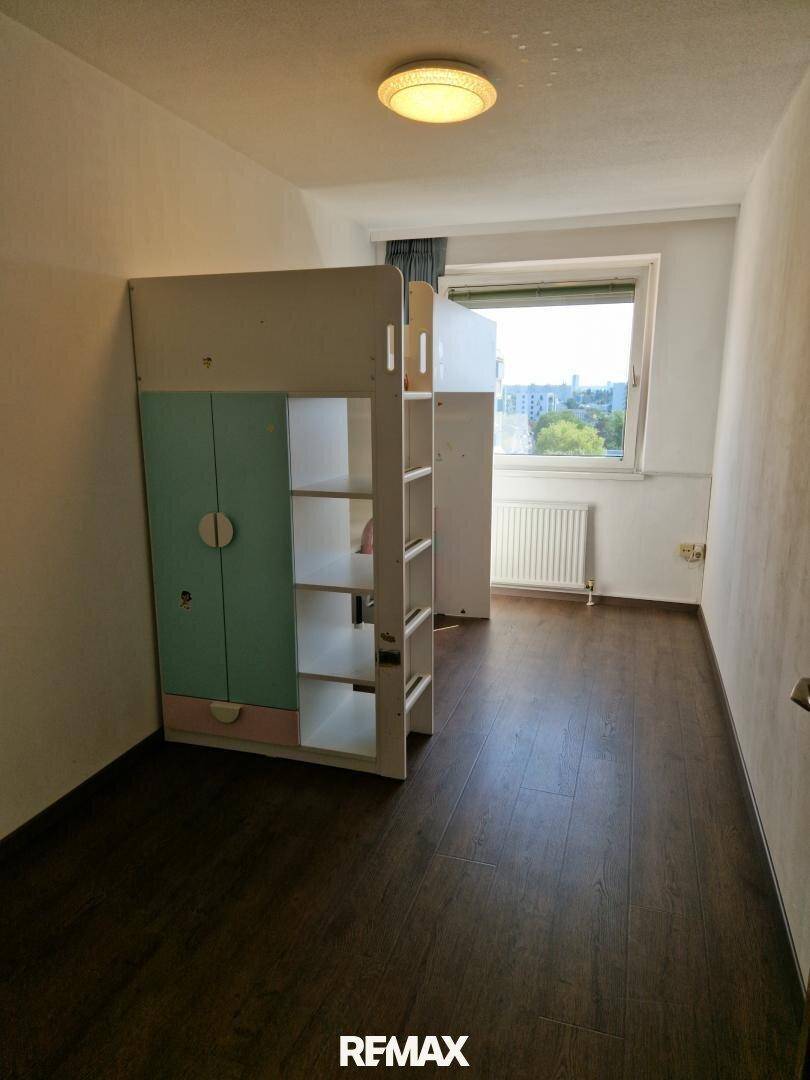 Kinderzimmer mit Hochbett und Stauraum, dunklem Laminatboden und Fenster für Tageslicht.