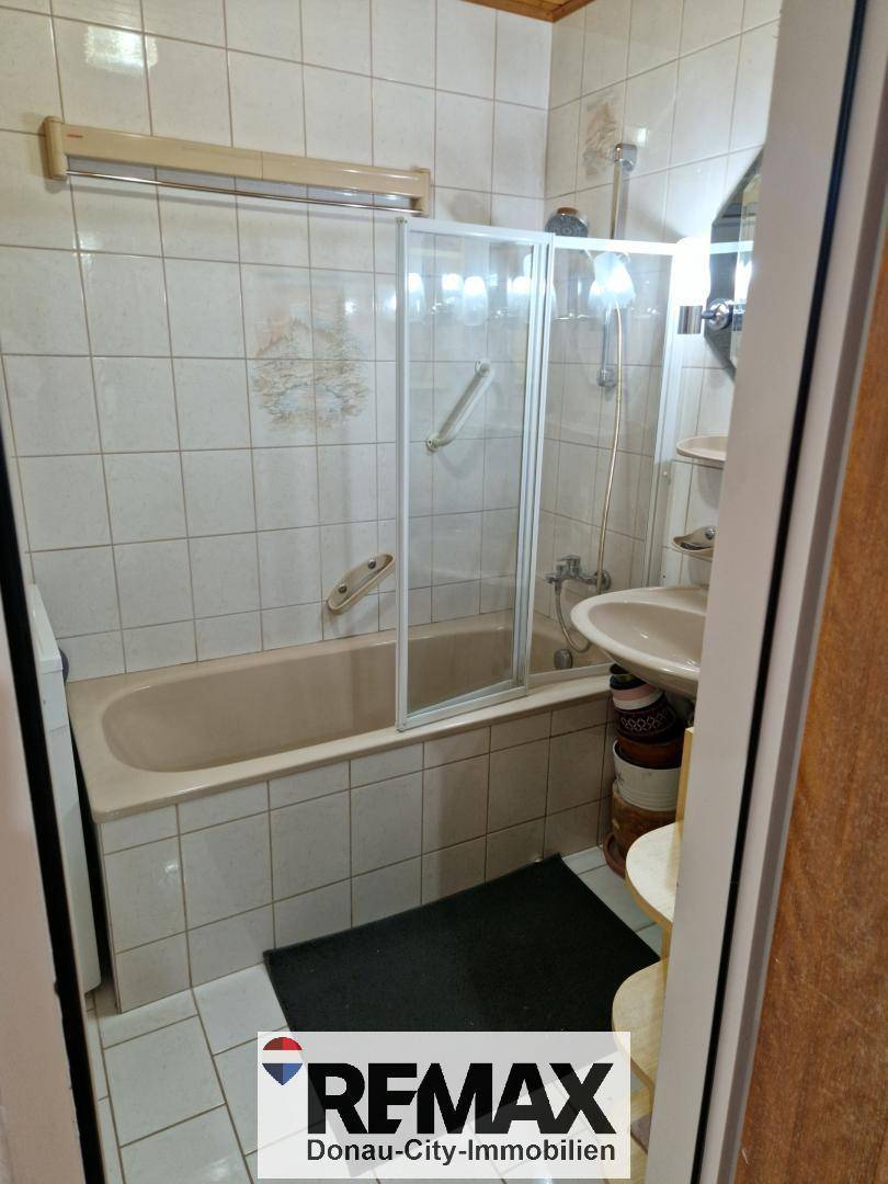 Badezimmer mit Badewanne, Duschabtrennung und Waschbecken, hell gefliest in neutralen Farben.