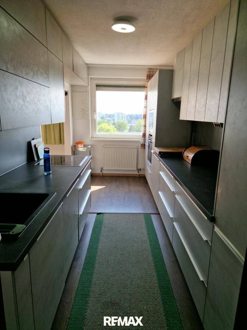 Schmale Küche mit modernen grauen Schränken, dunkler Arbeitsplatte und Fenster mit Ausblick.