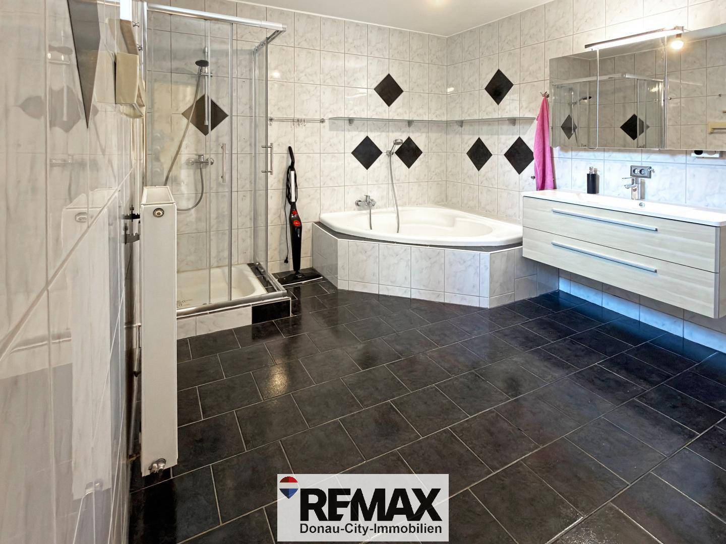 Gefliestes Badezimmer mit Eckbadewanne, Duschkabine und modernem Waschtisch.