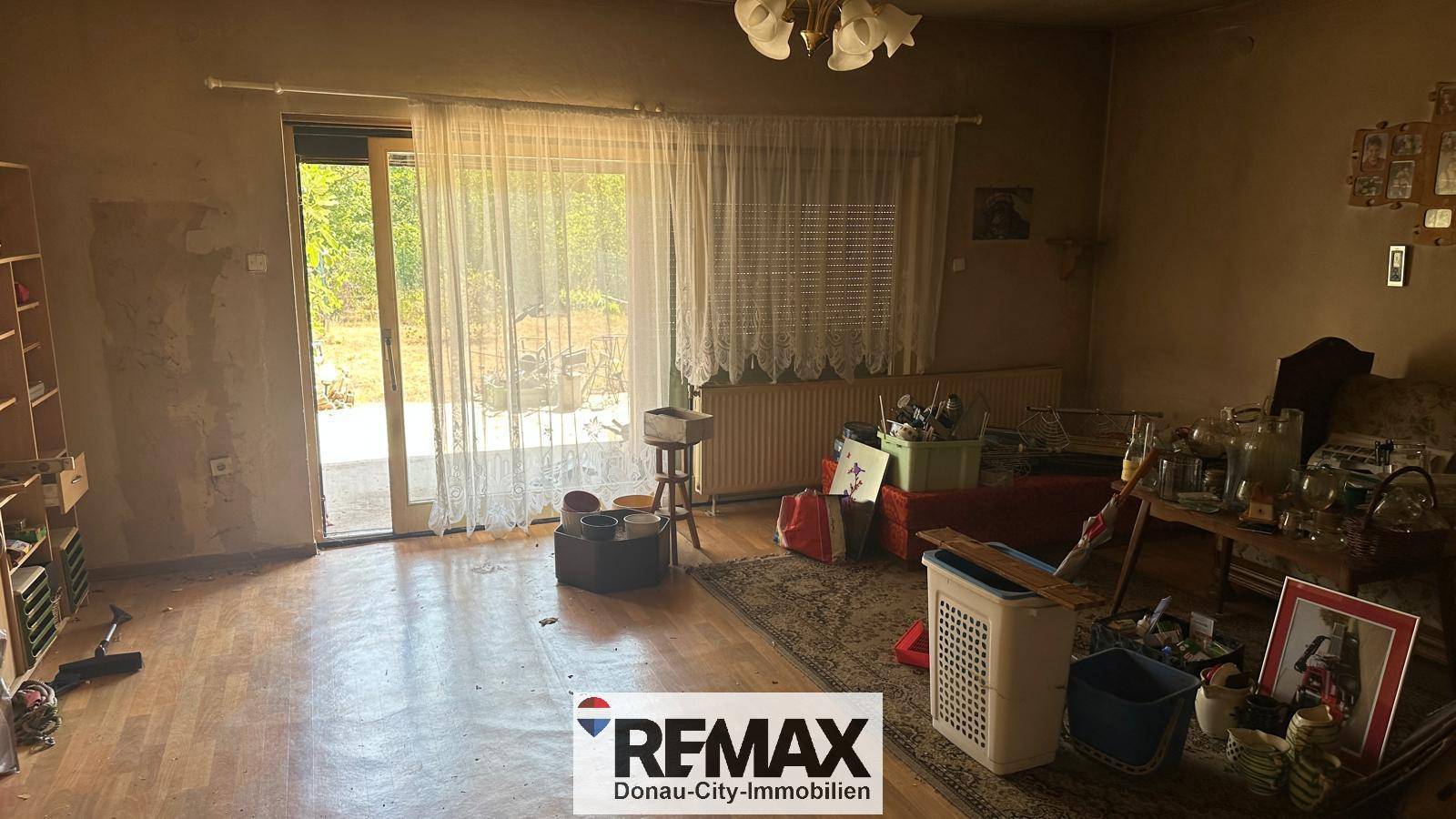 Renovierungsbedürftiges Wohnzimmer mit Terrassenzugang und sichtbaren Abnutzungsspuren.