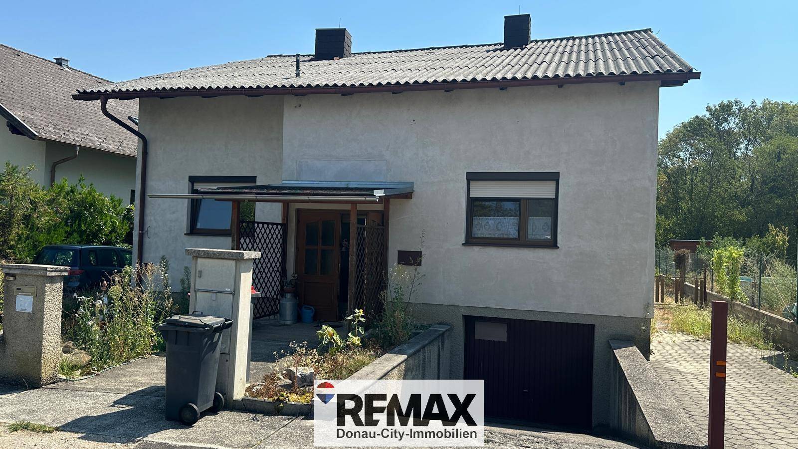 Vorderansicht des Hauses mit integrierter Garage und Zufahrt, umgeben von Vegetation.