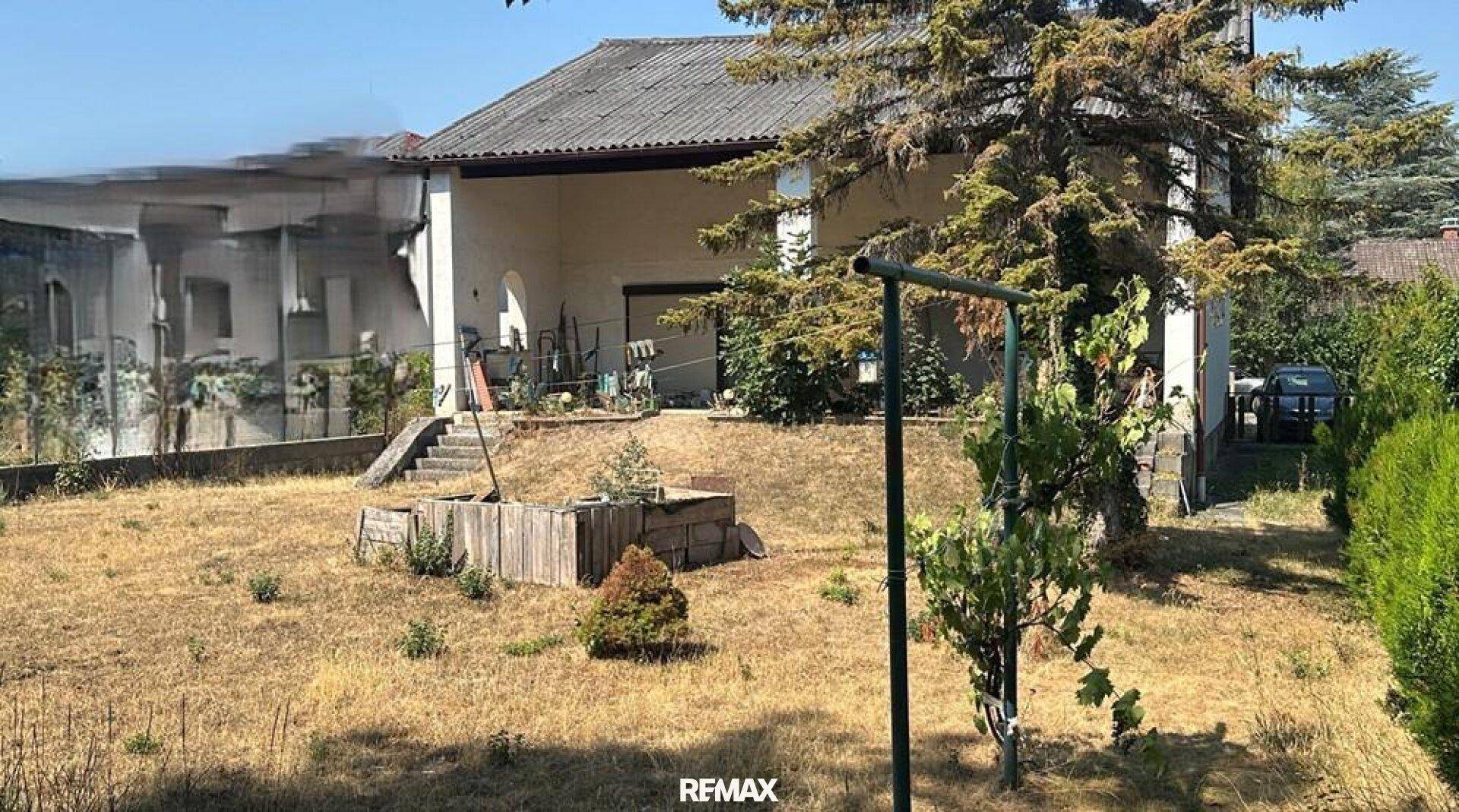 Hinteransicht des Hauses mit überdachter Terrasse und großem, trockenem Garten.