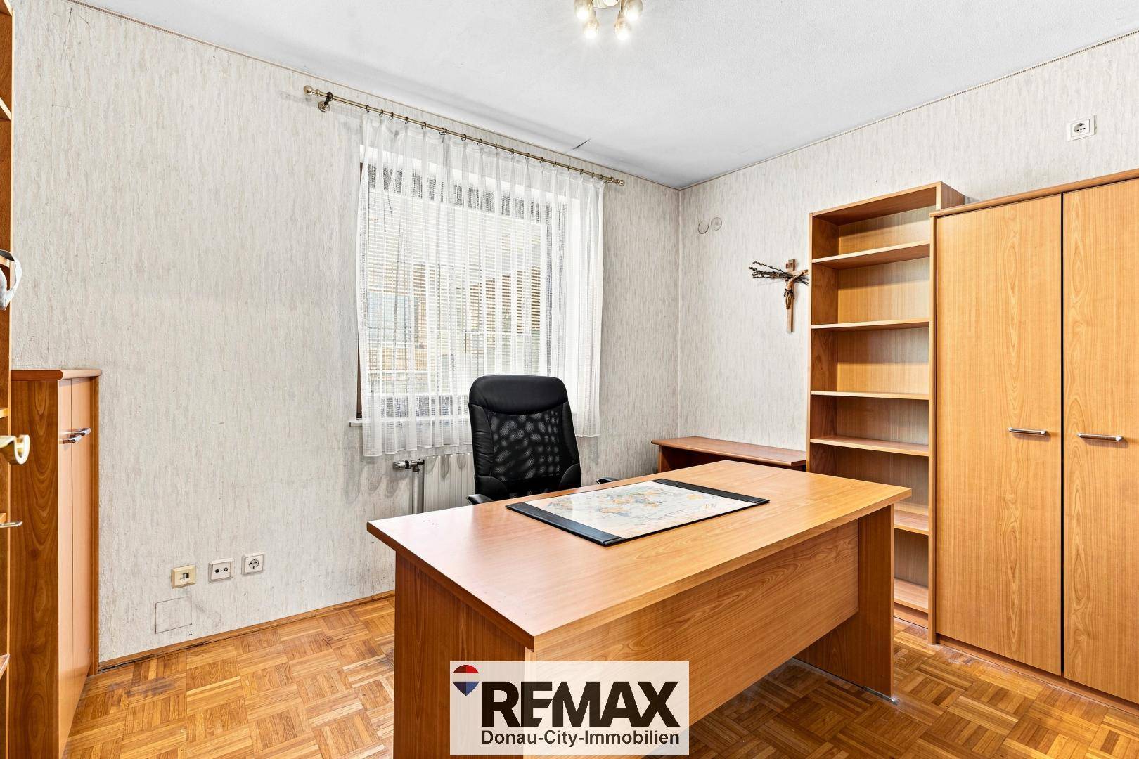 Arbeitszimmer mit Parkettboden, Schreibtisch und Regalen.