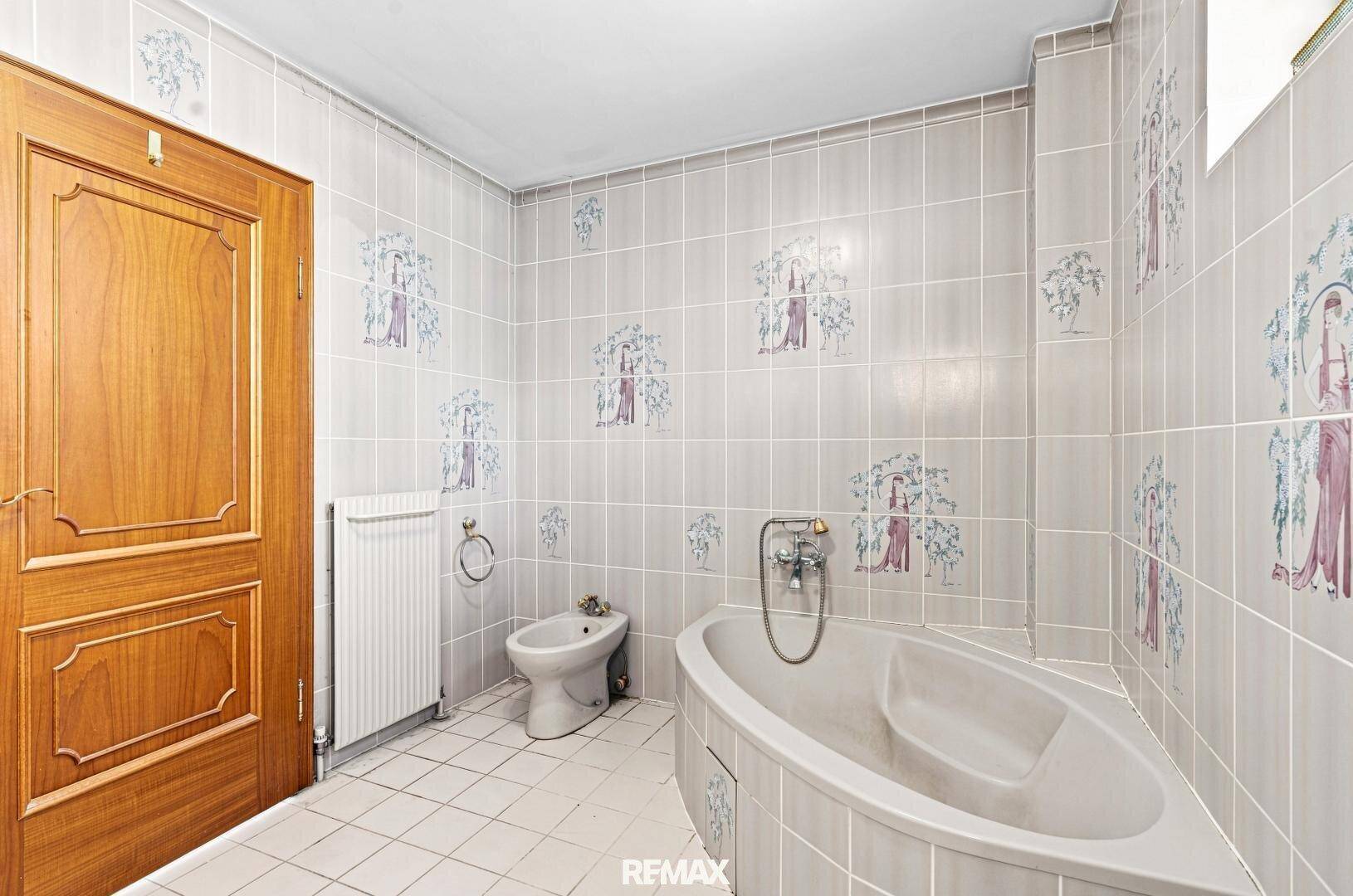 Badezimmer mit Badewanne, Bidet und hellgrauen Fliesen mit dekorativen Mustern.
