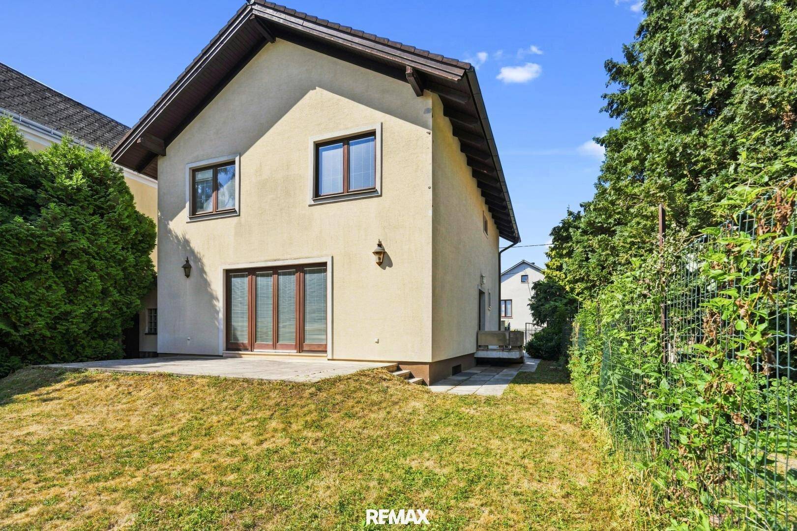 Seitenansicht des Hauses mit Zugang zum Garten und einer kleinen gepflasterten Fläche.