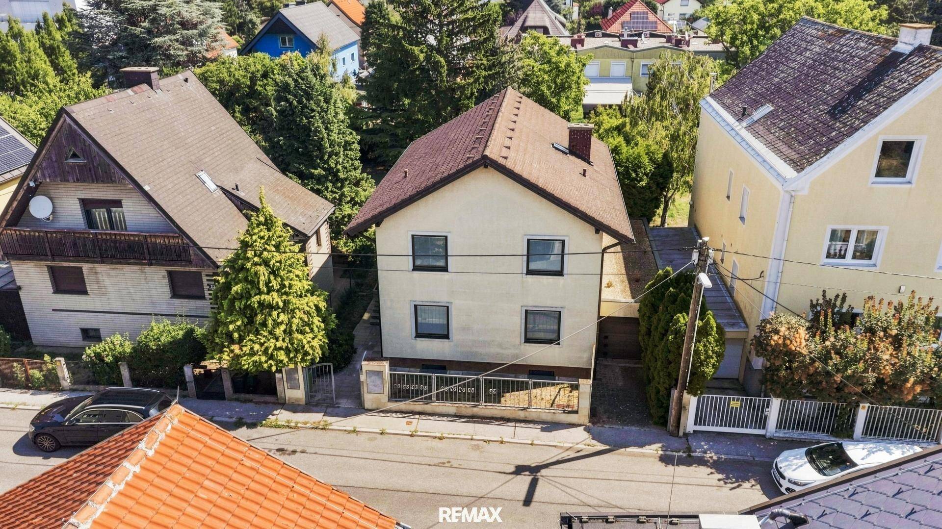 Luftaufnahme der Hausfront und der Straße mit angrenzenden Nachbargebäuden und Bäumen.