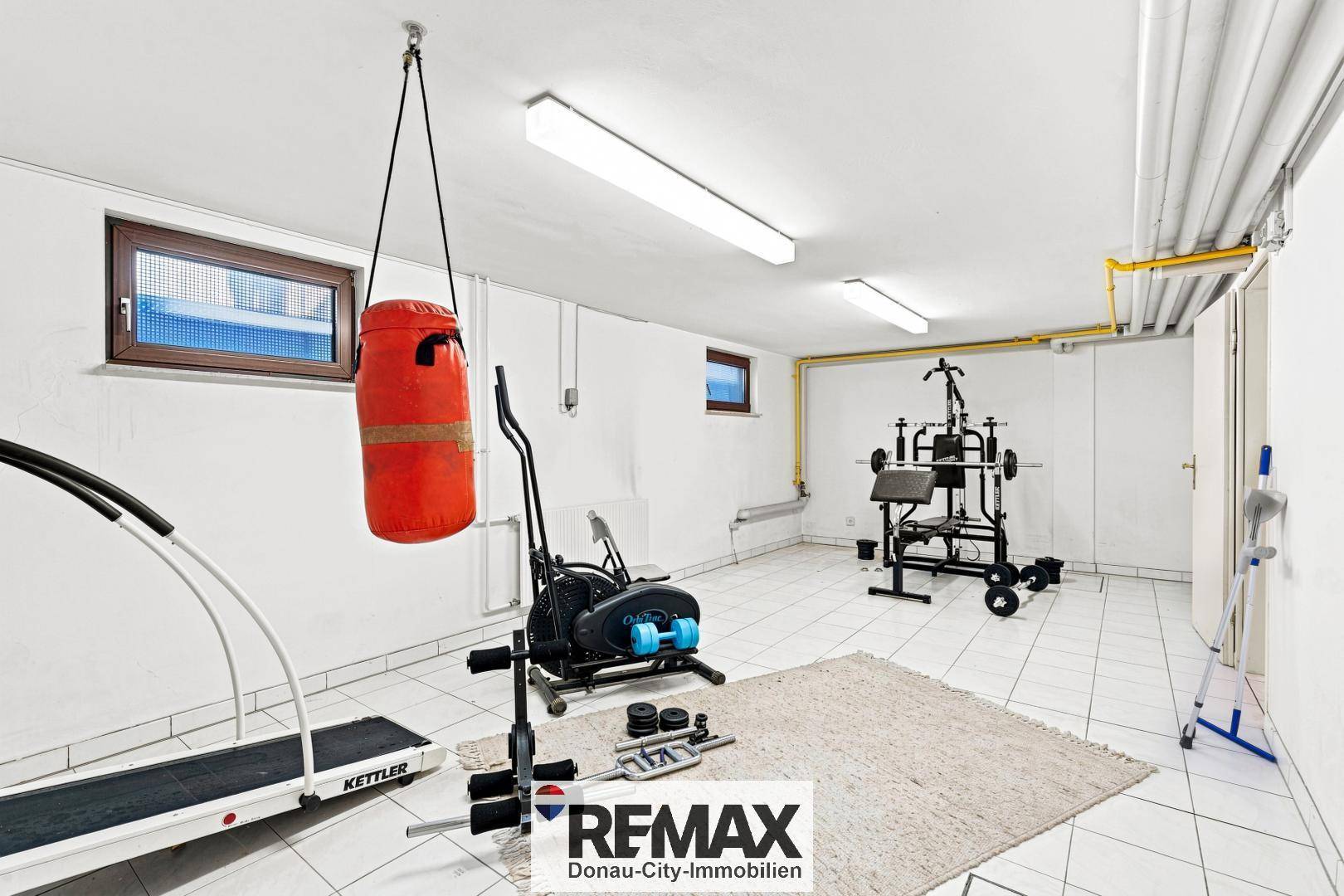 Fitnessraum im Keller mit verschiedenen Trainingsgeräten und Fliesenboden.