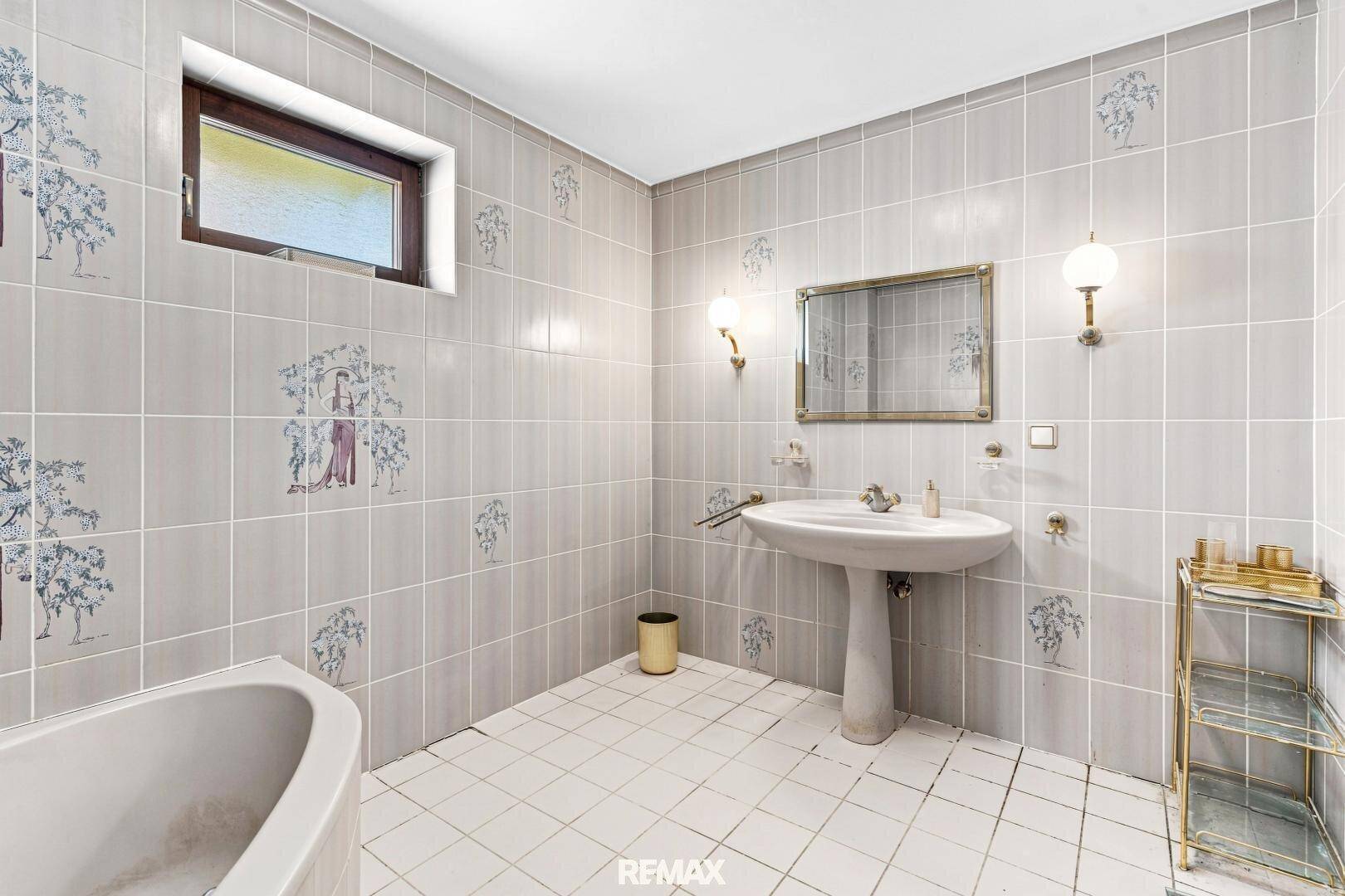 Badezimmer mit Badewanne, Waschbecken und hellgrauen Fliesen mit dekorativen Mustern.