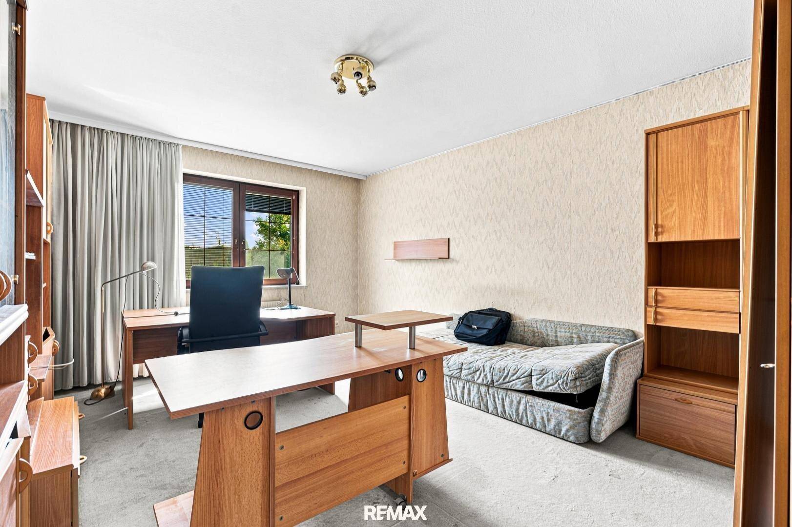 Helles Arbeitszimmer mit Teppichboden, Holzmöbeln und einem Fenster mit Blick ins Grüne.