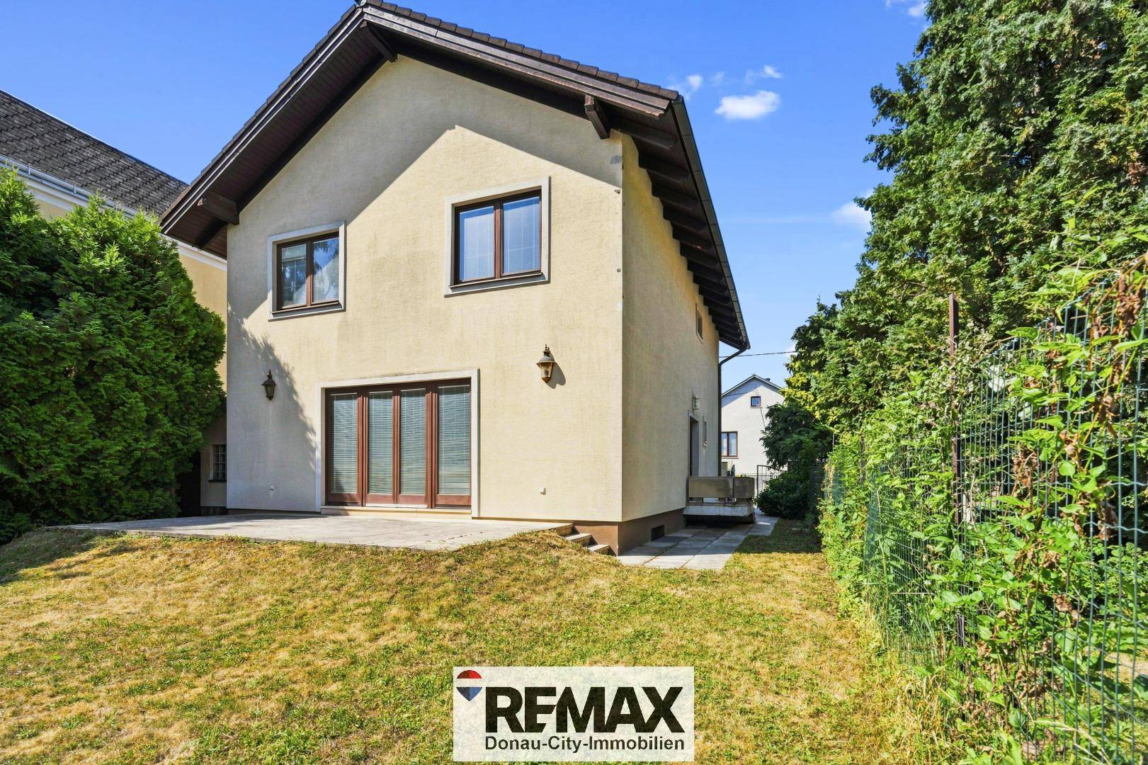 Seitliche Ansicht des Hauses mit kleiner gepflasterter Terrasse und Zugang zum Garten.