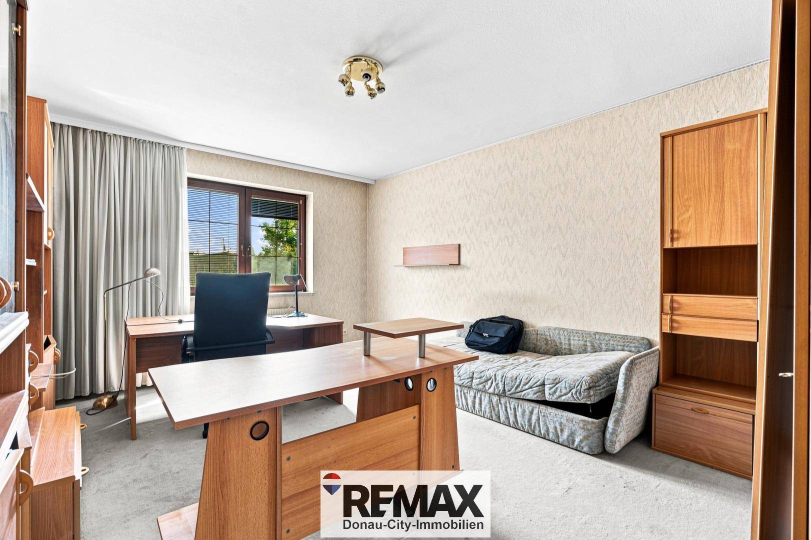 Helles Arbeitszimmer mit Teppichboden, Schreibtisch und Blick ins Grüne.