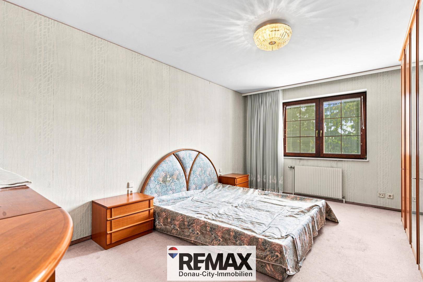 Schlafzimmer mit Teppichboden, Doppelbett und Fenster mit Blick ins Grüne.