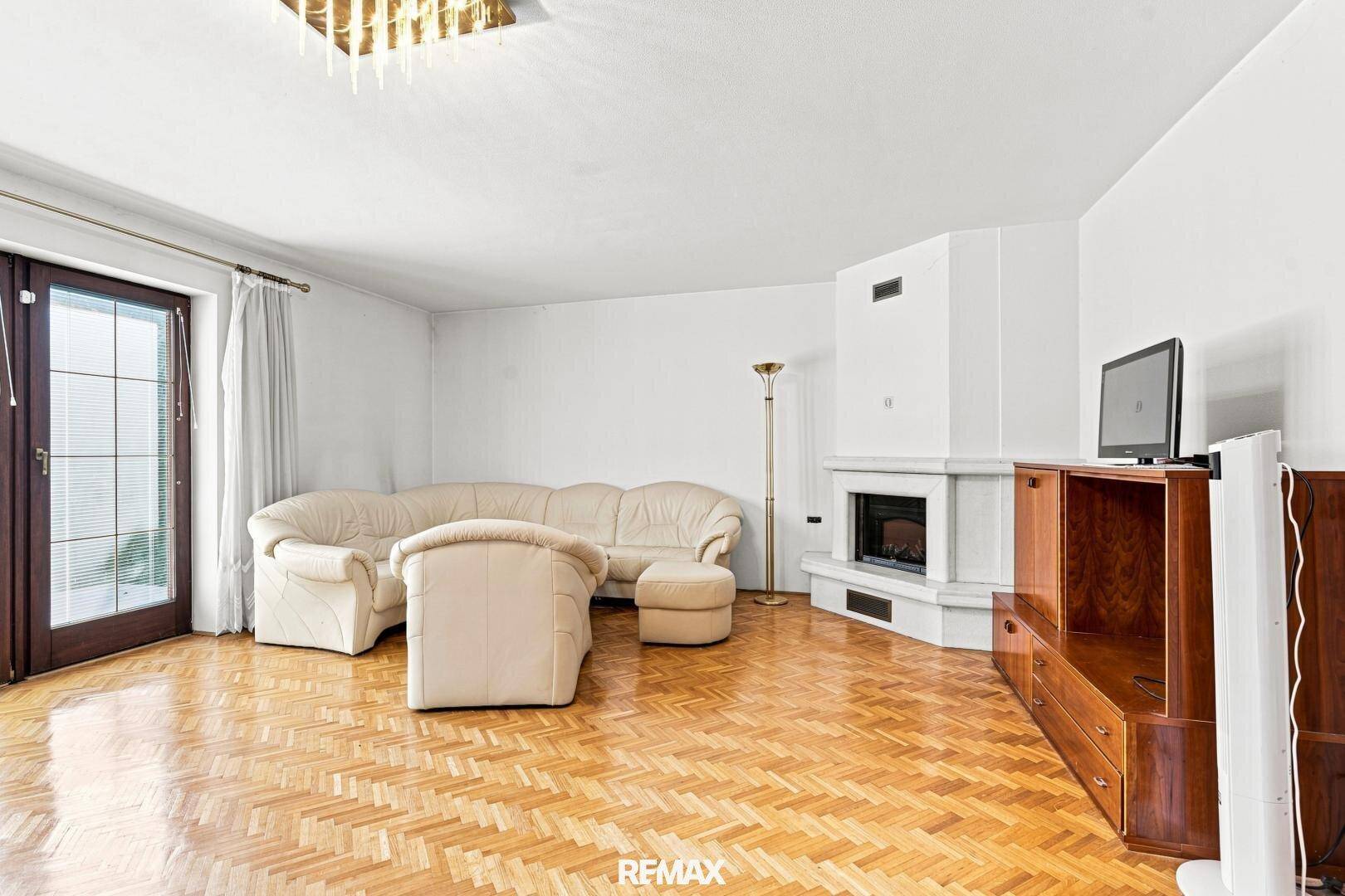 Helles Wohnzimmer mit Parkettboden, Kamin und Zugang zum Außenbereich.