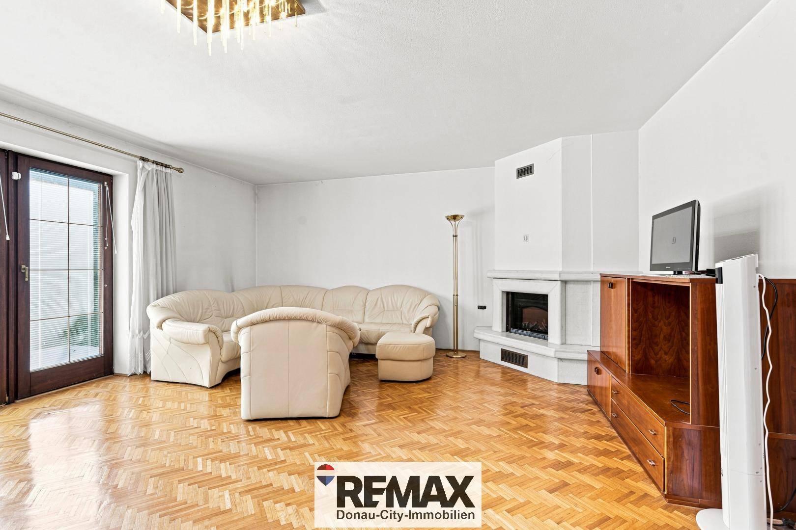 Helles Wohnzimmer mit Parkettboden, Kamin und Zugang zur Terrasse.