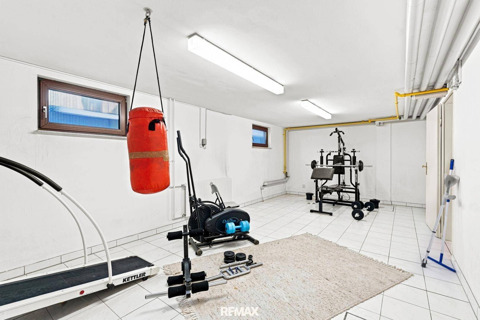 Fitnessraum im Keller mit verschiedenen Trainingsgeräten und Fliesenboden.