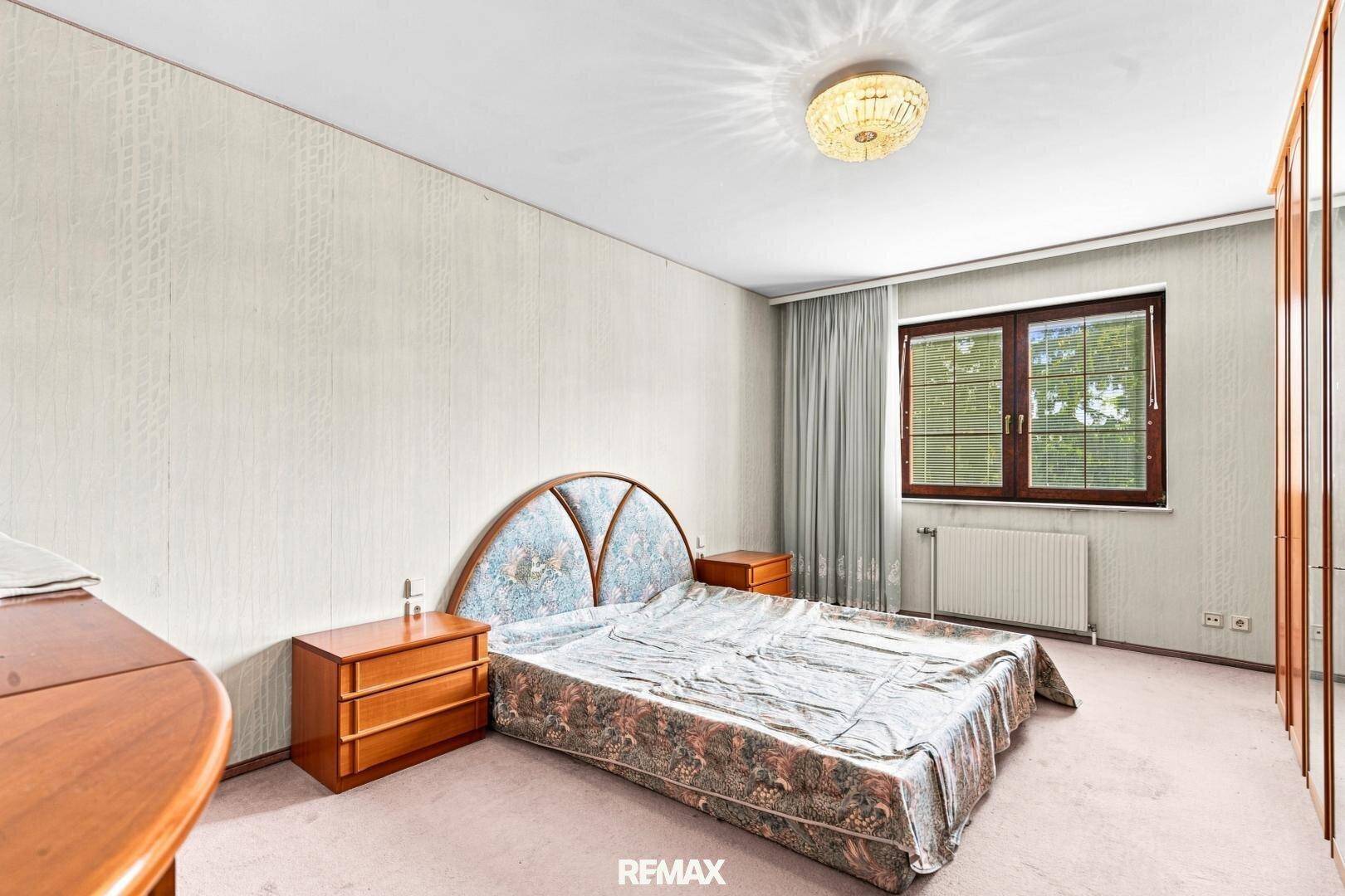 Schlafzimmer mit Teppichboden, gemusterter Tapete und einem Fenster mit Blick ins Grüne.