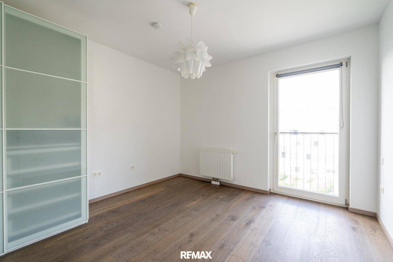 Helles Schlafzimmer mit Holzboden, modernem Kleiderschrank und französischem Balkon.