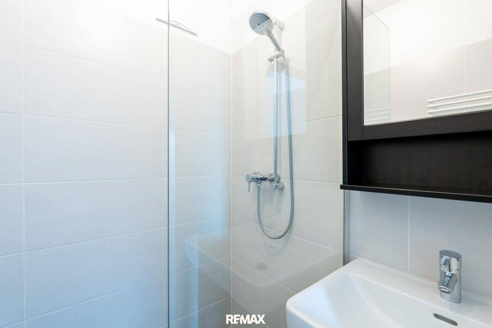 Detailansicht der ebenerdigen Dusche und des Waschbeckens im modernen Badezimmer.
