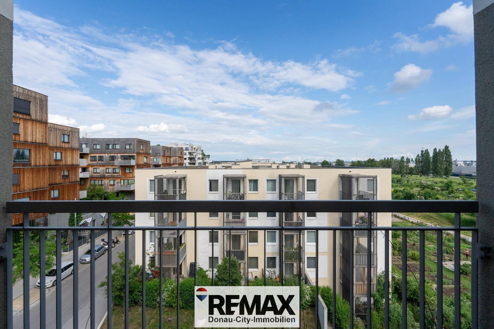 Ausblick vom Balkon auf moderne Wohngebäude, eine Straße und grüne Umgebung.