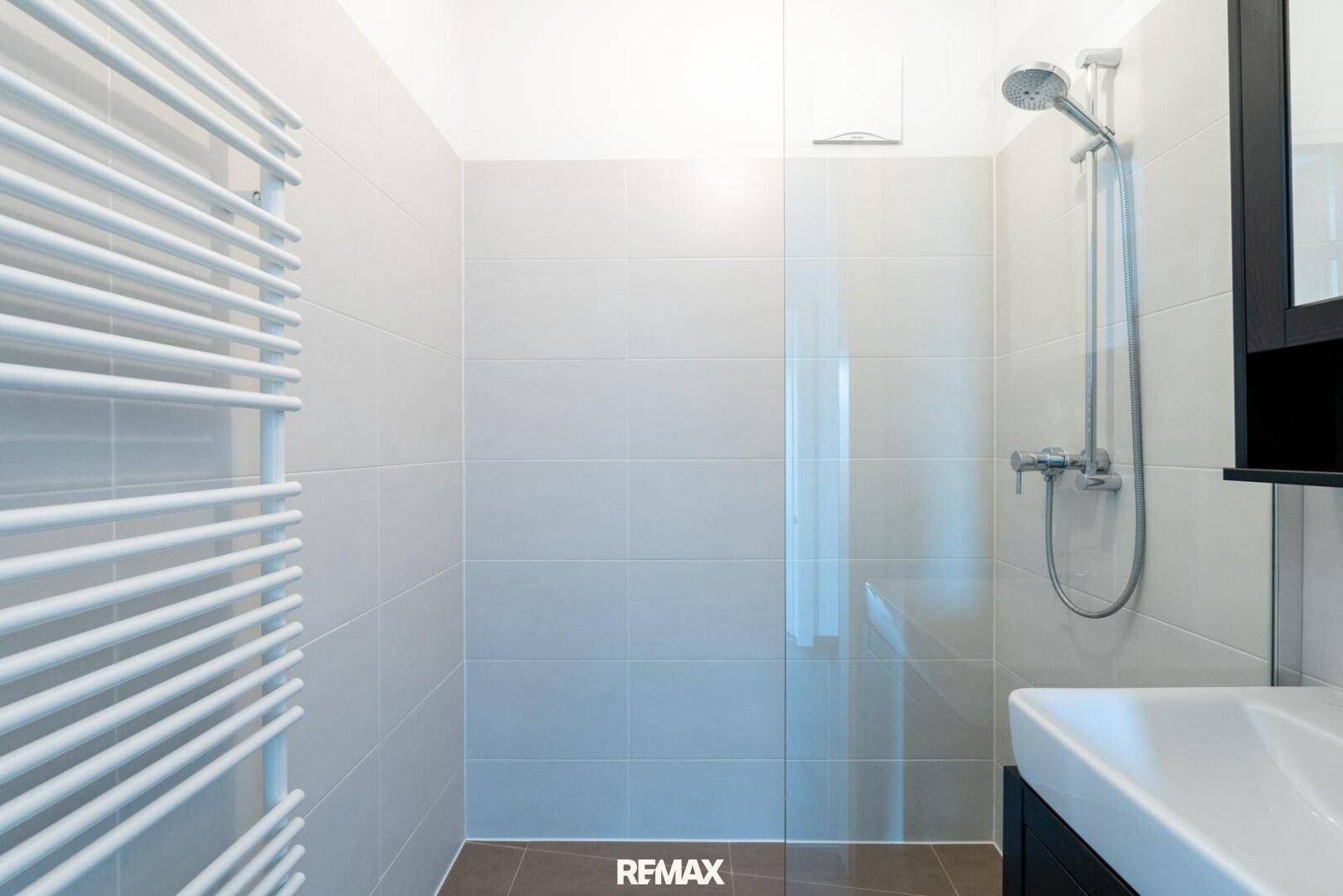 Modernes Badezimmer mit ebenerdiger Dusche, beheiztem Handtuchhalter und Einzelwaschbecken.