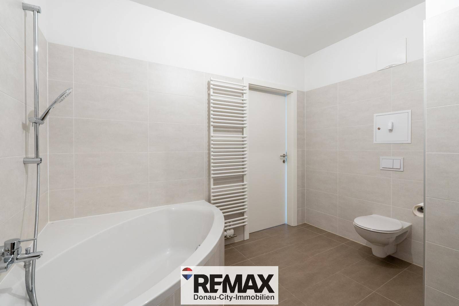 Badezimmer mit wandhängendem WC, beheiztem Handtuchhalter und moderner Eckbadewanne.